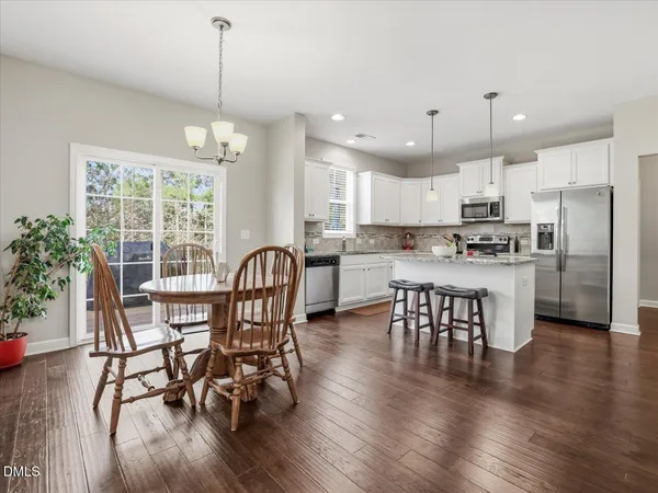 a kitchen with stainless steel appliances granite countertop a stove a refrigerator a kitchen island a dining table and chairs with wooden floor