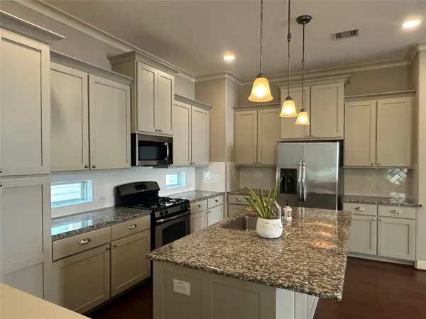 a kitchen with stainless steel appliances kitchen island granite countertop a stove a refrigerator a sink a oven and white cabinets with wooden floor