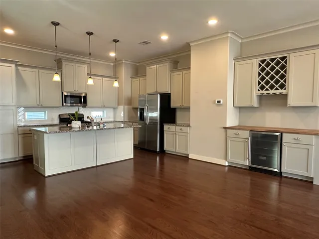 a kitchen with stainless steel appliances kitchen island granite countertop a stove a refrigerator a sink a oven and white cabinets with wooden floor