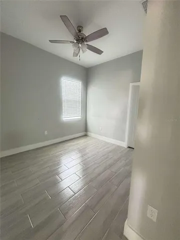 an empty room with wooden floor fan and windows