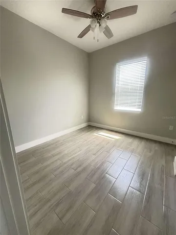 an empty room with wooden floor fan and windows