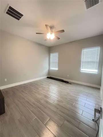 an empty room with wooden floor chandelier fan and windows