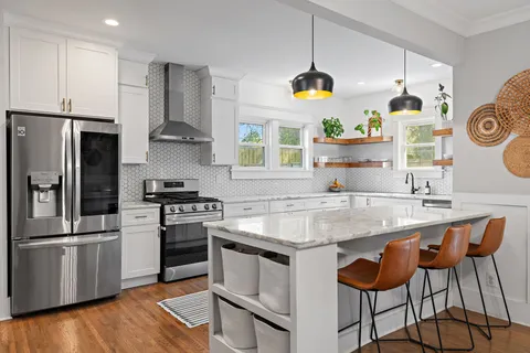 a kitchen with stainless steel appliances granite countertop a sink a stove a refrigerator and island with wooden floor