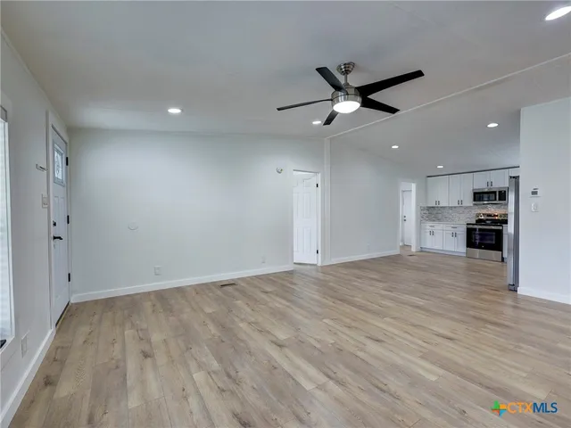 an empty room with wooden floor a ceiling fan and kitchen view