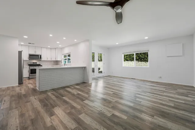 a view of kitchen and empty room with wooden floor and windows