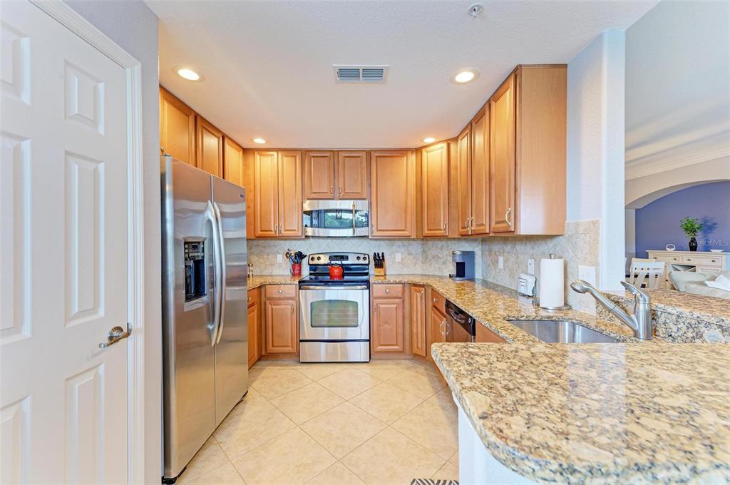424 Winding Brook Lane, Unit 104 Bradenton, FL 34212 - Photo 11 of 72 a kitchen with stainless steel appliances granite countertop a refrigerator oven a sink dishwasher and wooden cabinets with wooden floor