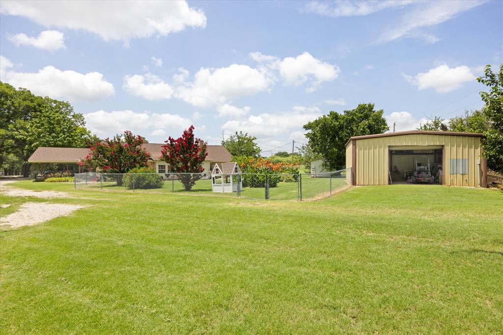 4210 Waples Road Granbury, TX 76049 - Photo 11 of 37 Expansive green lawn with a chain-link fence, detached metal storage building, and a single-story residence featuring a covered porch