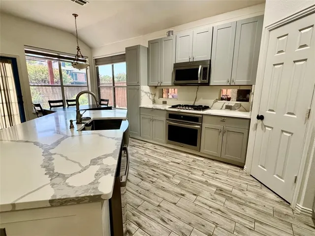 a kitchen with stainless steel appliances granite countertop a stove top oven a sink dishwasher a dining table and chairs with wooden floor