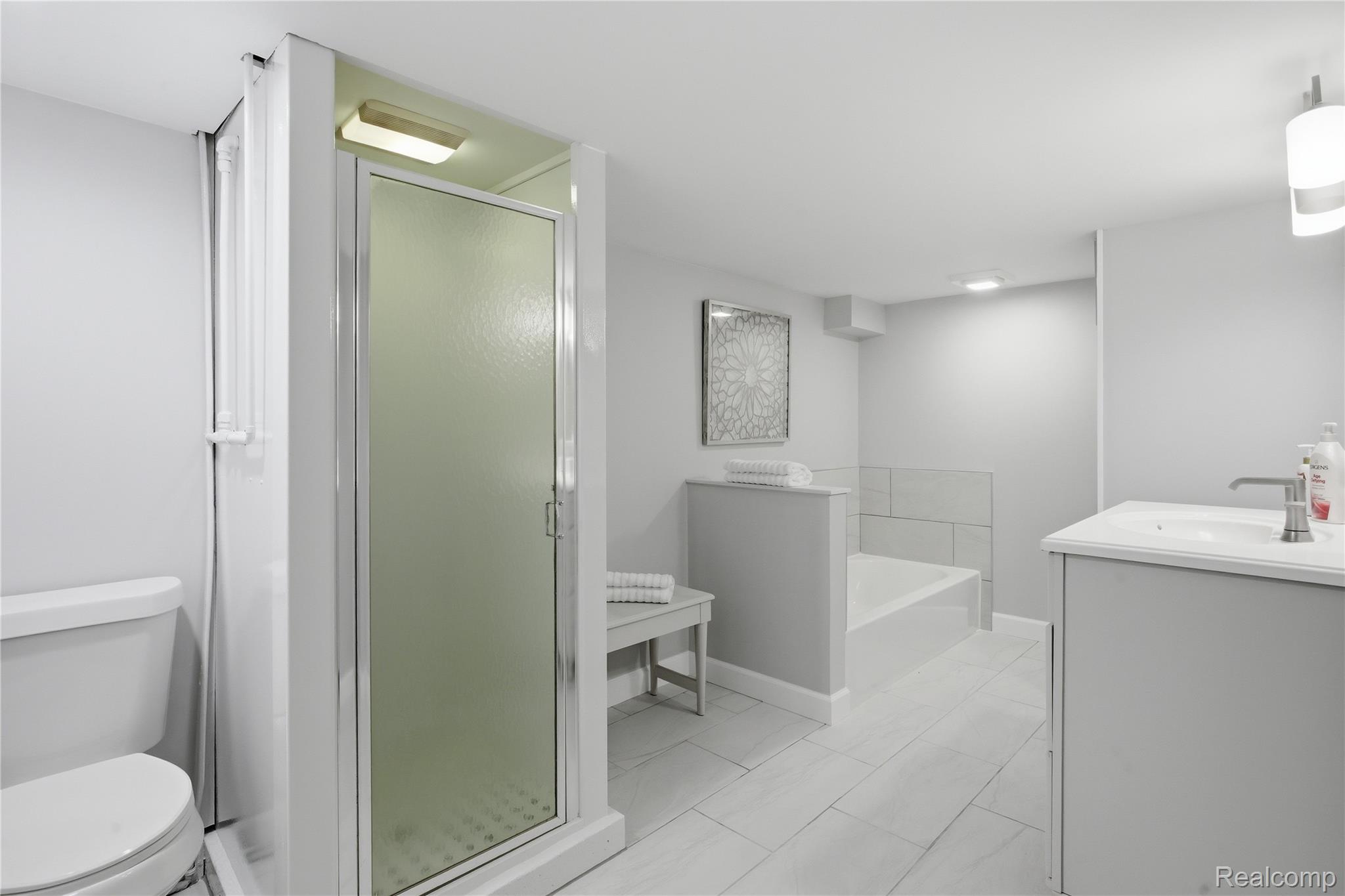 37257 Dundee Street Sterling Heights, MI 48310 - Photo 24 of 47 Bathroom featuring a glass-enclosed shower, a built-in soaking tub, a single vanity with an integrated sink, a wall-mounted light fixture, and wood-finish tile flooring