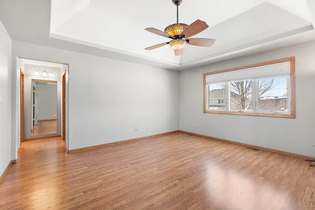 an empty room with wooden floor chandelier fan and windows