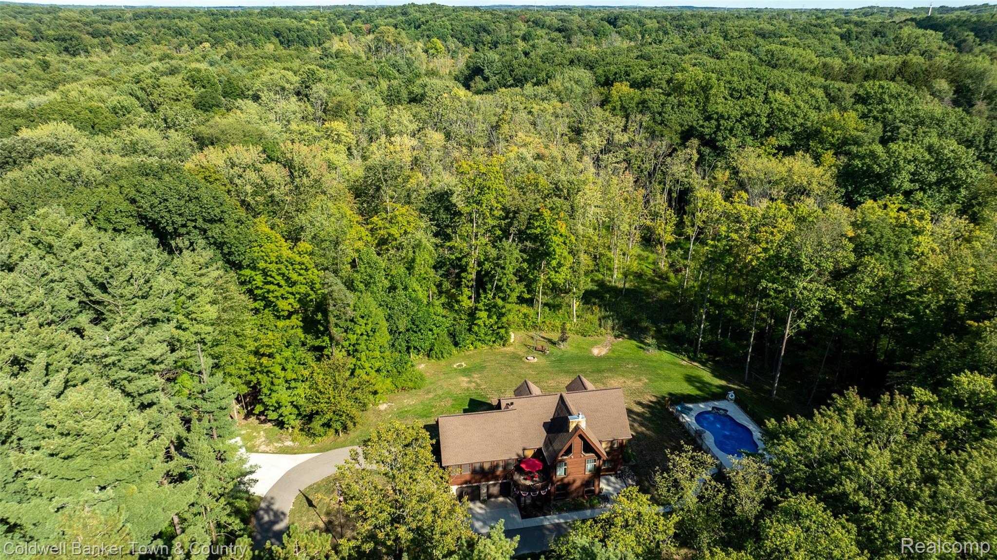 7023 Munsell Road Howell, MI 48843 - Photo 47 of 55 Expansive wooded surroundings with a private outdoor pool, multi-level dwelling with a brown shingle roof, and a paved driveway