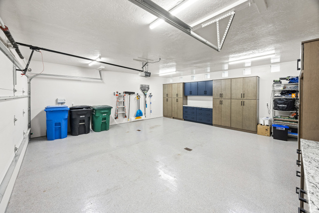 1774 Country Club Drive Logan, UT 84321 - Photo 14 of 28 Spacious garage featuring an epoxy-coated floor, integrated cabinetry, ample overhead lighting, and an automatic garage door opener