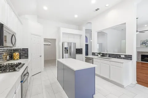 a large kitchen with stainless steel appliances a stove a sink a refrigerator and white cabinets with wooden floor