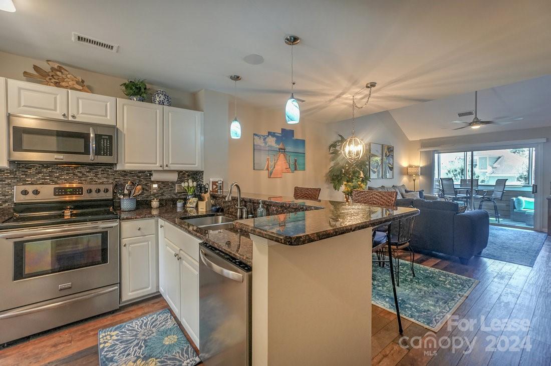 17542 Tuscany Lane Cornelius, NC 28031 - Photo 3 of 35 a kitchen with stainless steel appliances granite countertop a stove top oven a sink dishwasher a dining table and chairs with wooden floor
