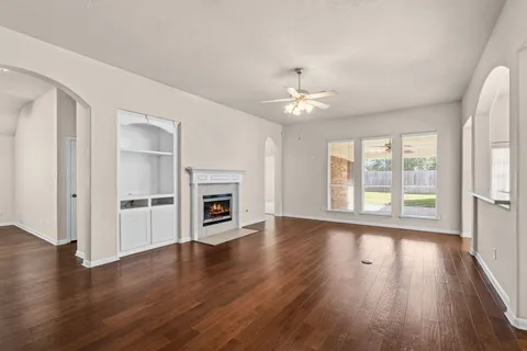 an empty room with wooden floor fireplace and windows