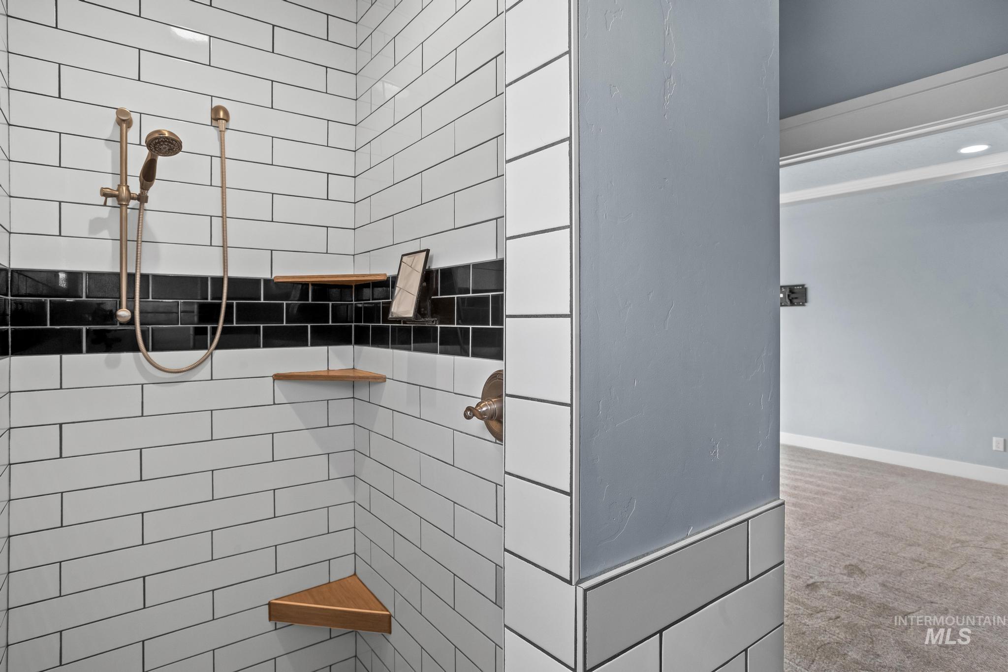 2681 East Rhyolite Court Nampa, ID 83686 - Photo 28 of 48 Shower stall featuring white subway tile with a black accent band, a bronze-finish shower head with handheld sprayer, and built-in wood corner shelves