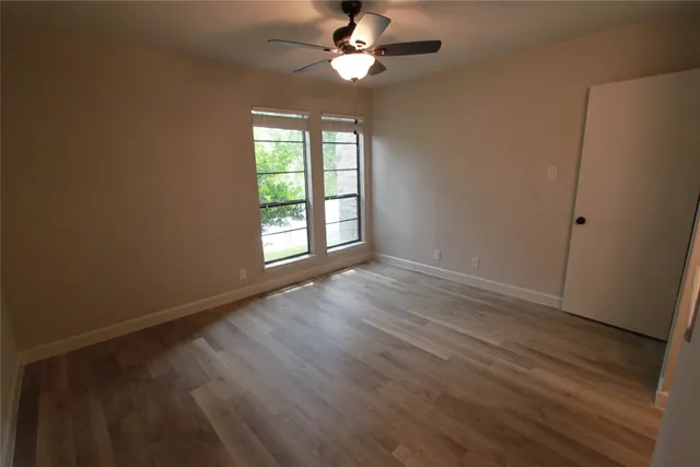 an empty room with wooden floor chandelier fan and windows
