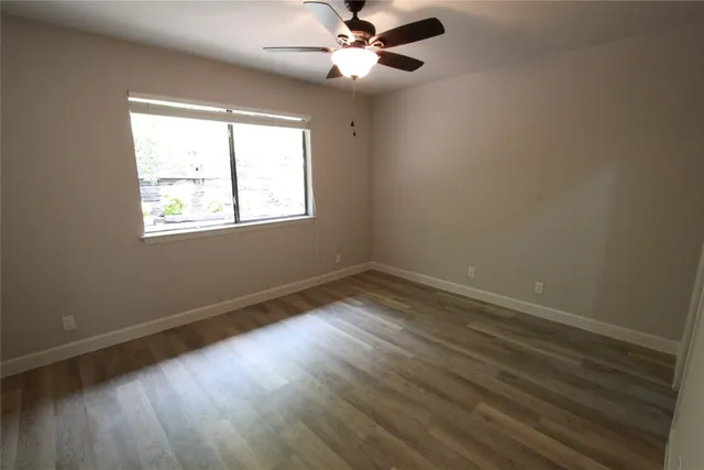 an empty room with wooden floor ceiling fan and windows