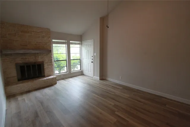 an empty room with wooden floor fireplace and windows