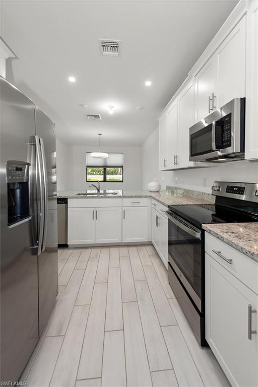 7546 Rockefeller Drive Naples, FL 34119 - Photo 13 of 31 Kitchen featuring stainless steel appliances, white cabinets, recessed lighting, light stone counters, and light wood-style flooring