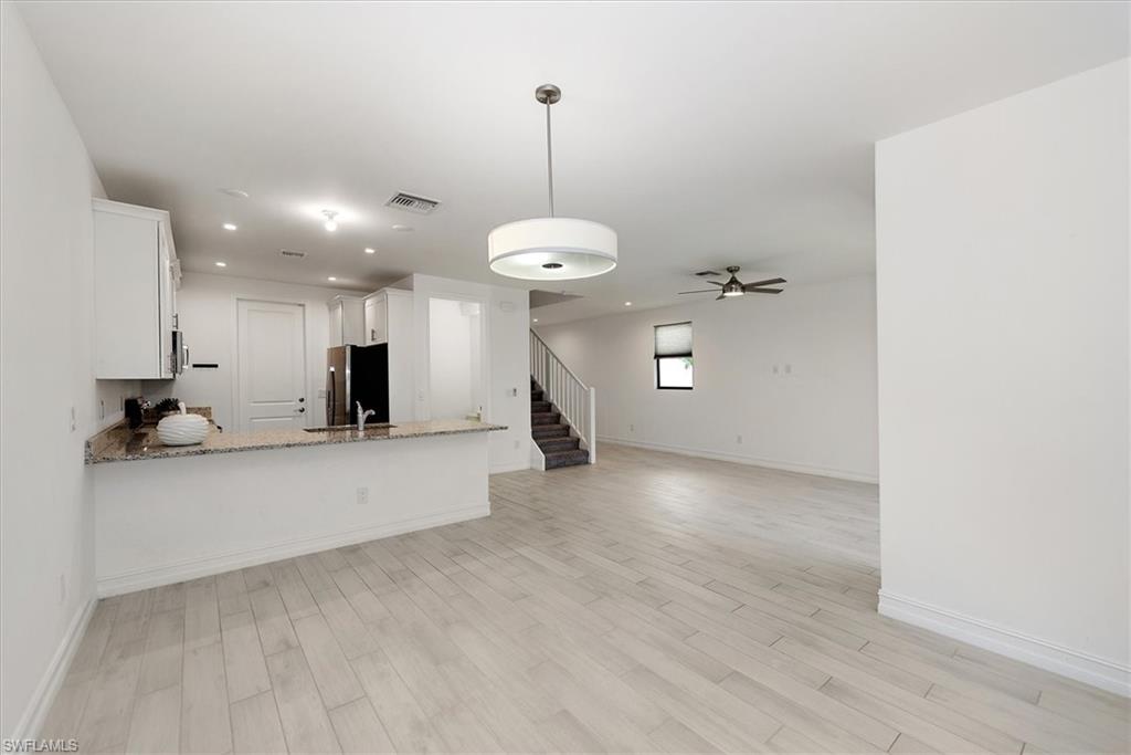 7546 Rockefeller Drive Naples, FL 34119 - Photo 31 of 31 Kitchen featuring white cabinets, light stone countertops, light wood-style flooring, open floor plan, and a peninsula