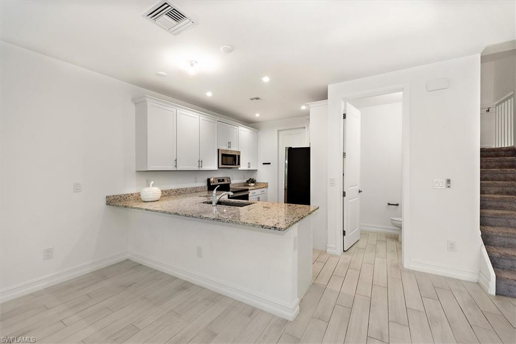 7546 Rockefeller Drive Naples, FL 34119 - Photo 10 of 31 Kitchen featuring a peninsula, light stone countertops, appliances with stainless steel finishes, light wood finished floors, and recessed lighting