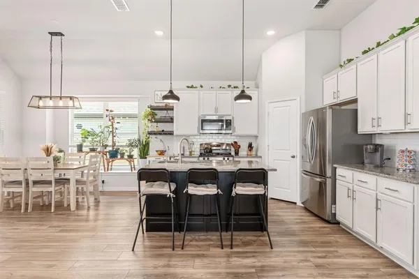 a kitchen with stainless steel appliances kitchen island granite countertop a table chairs stove and white cabinets