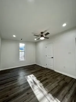 an empty room with wooden floor window and ceiling fan