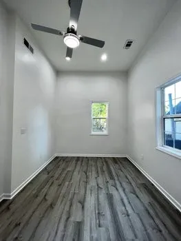 an empty room with wooden floor chandelier fan and windows