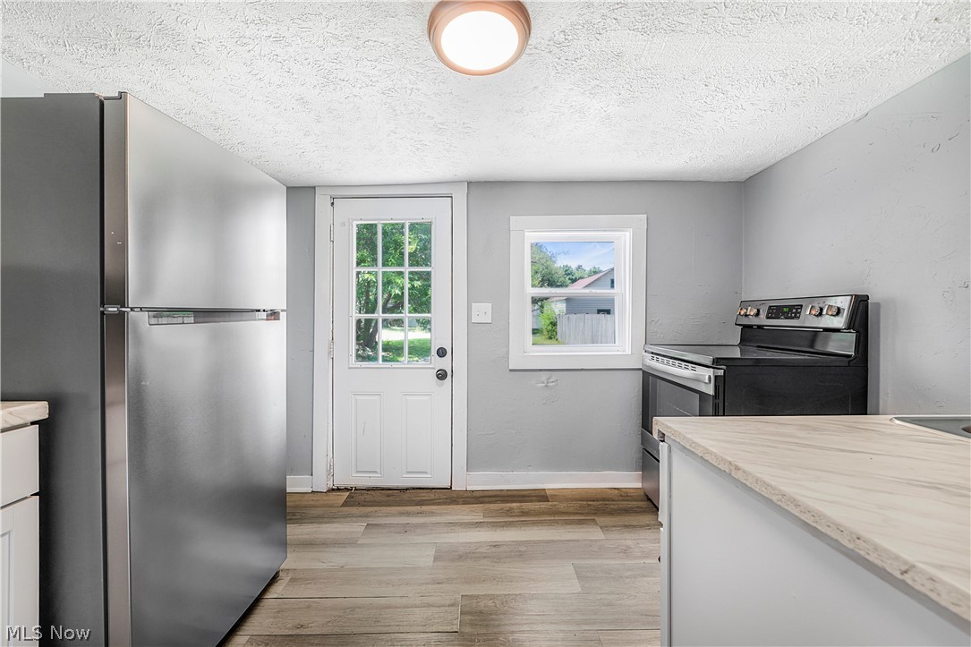 885 Wales Road Northeast Massillon, OH 44646 - Photo 22 of 34 Kitchen featuring stainless steel refrigerator, black electric range, wood-finish flooring, light-toned countertops, and a white paneled door with glass inserts