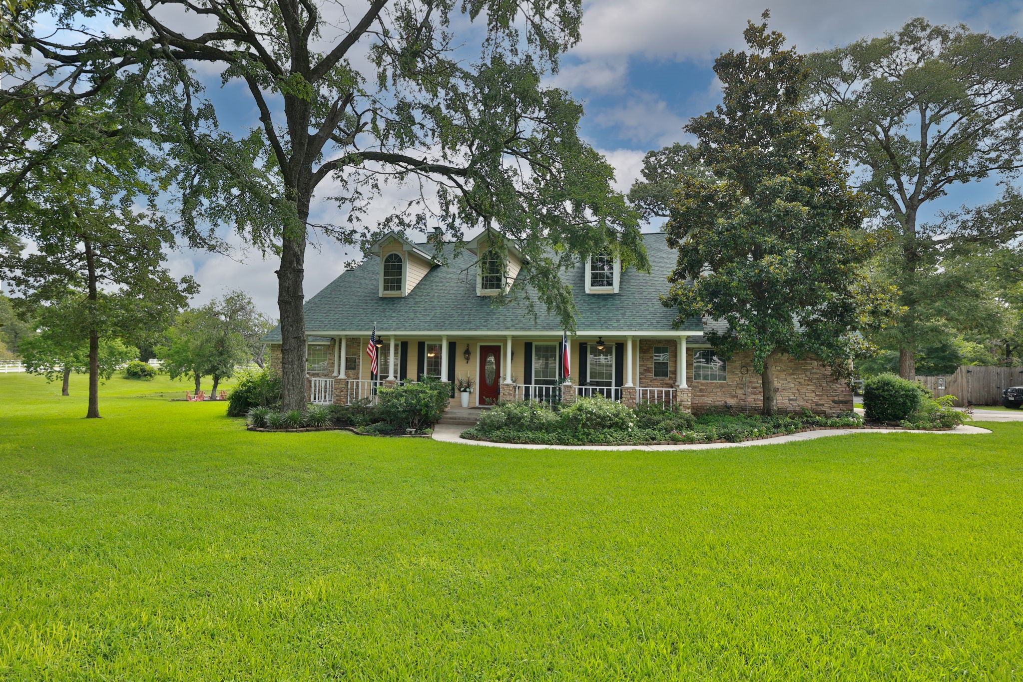 34310 High Point Drive Magnolia, TX 77355 - Photo 3 of 48 Charming two-story home with a classic front porch, nestled among mature trees and lush green lawn. Perfect for peaceful living with ample outdoor space.