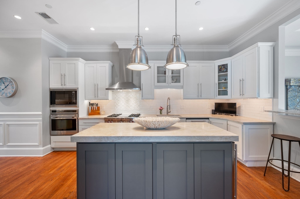 221 Victory Road, Unit 221 Quincy, MA 02171 - Photo 4 of 34 a kitchen with stainless steel appliances kitchen island granite countertop a sink dishwasher a stove and a dining table with wooden floor