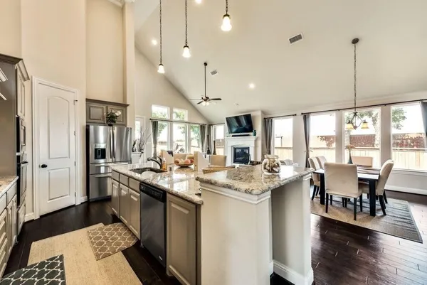 a room with stainless steel appliances kitchen island granite countertop a stove a sink a dining table and chairs with wooden floor