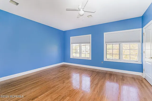 an empty room with wooden floor chandelier fan and windows