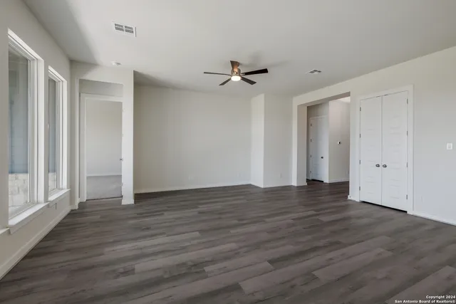 an empty room with wooden floor ceiling fan and windows