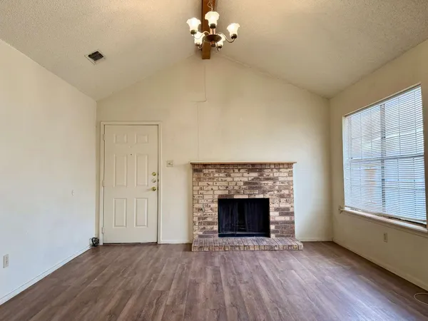 an empty room with wooden floor fireplace and windows