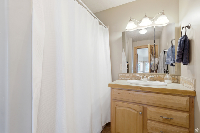 335 Bern Way Midway, UT 84049 - Photo 67 of 88 Bathroom vanity featuring a light wood-finish cabinet with storage, a countertop with a decorative tile backsplash, an integrated sink, and a framed mirror illuminated by a three-light fixture