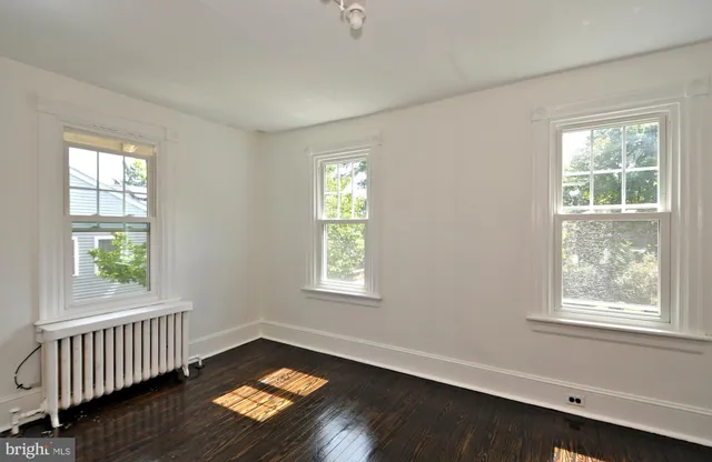 an empty room with wooden floor mirror and windows