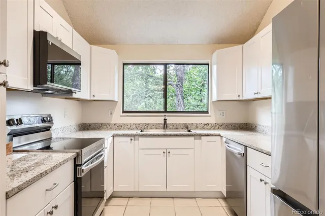 a kitchen with stainless steel appliances granite countertop white cabinets sink and window