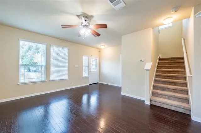 a view of an empty room with wooden floor and fan