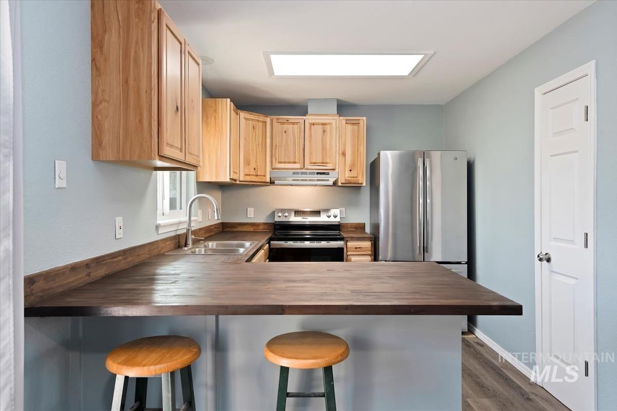 7091 West Limelight Street Boise, ID 83714 - Photo 10 of 34 Kitchen featuring light wood finish cabinets, a breakfast bar, a peninsula, stainless steel appliances, and dark wood-style floors
