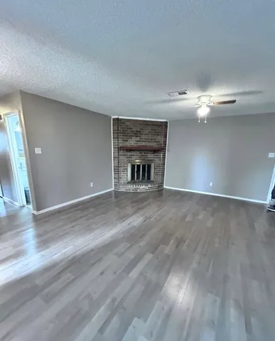 a view of an empty room with wooden floor fireplace and a window