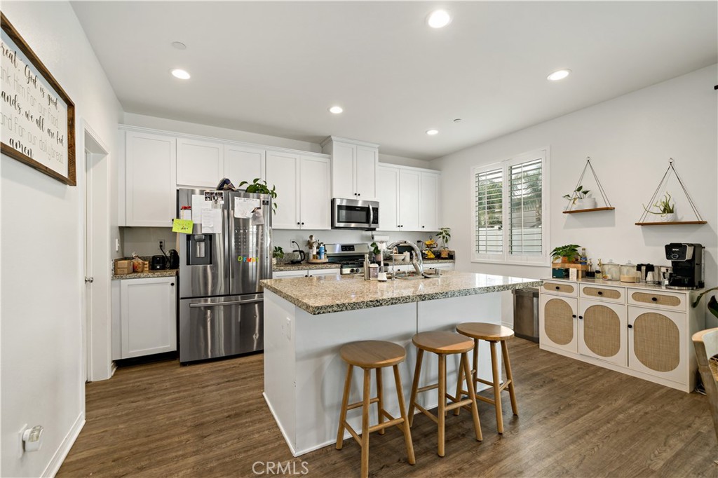30271 Ramsay Drive Menifee, CA 92584 - Photo 9 of 34 a kitchen with stainless steel appliances granite countertop a refrigerator a stove top oven a sink dishwasher and white cabinets with wooden floor