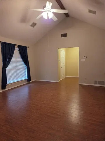 an empty room with wooden floor fan and windows