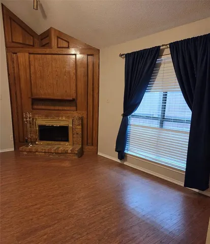 a view of an empty room with wooden floor fireplace and a window