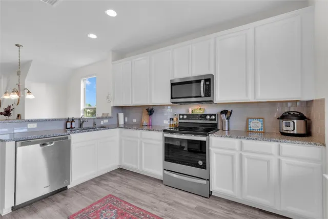 a kitchen with stainless steel appliances granite countertop a stove top oven a sink and white cabinets