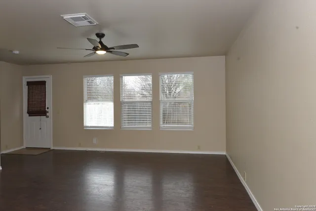 an empty room with wooden floor fan and windows