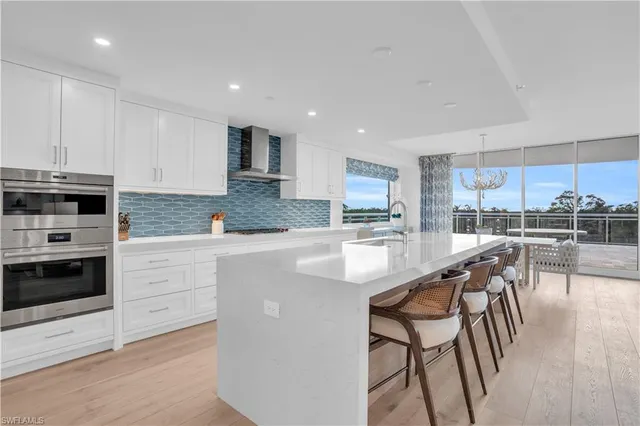 a kitchen with stainless steel appliances kitchen island granite countertop a stove a sink a oven a dining table and chairs with wooden floor