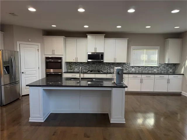 a kitchen with stainless steel appliances granite countertop a stove a sink a refrigerator and white cabinets