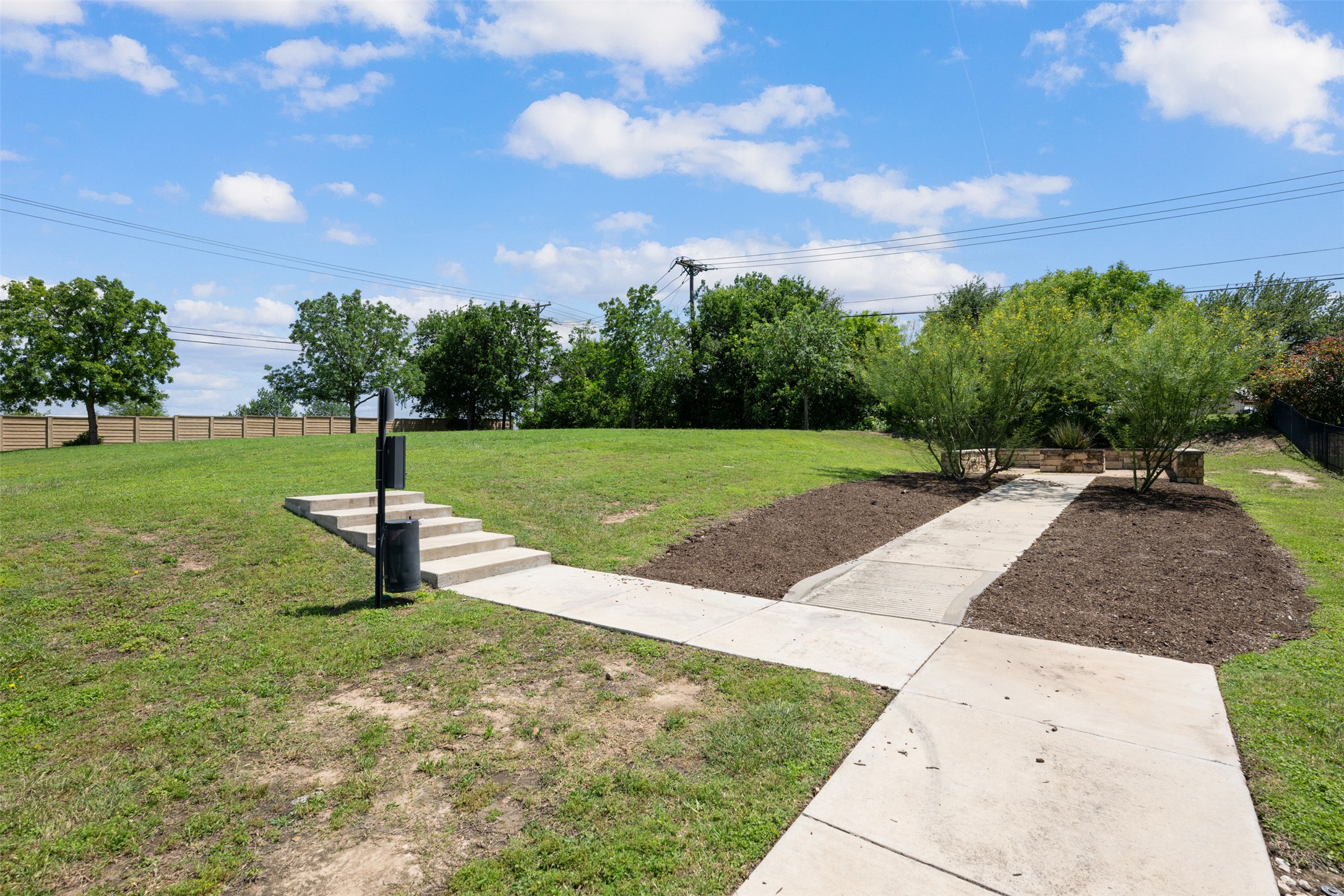 211 Parable Cove Pflugerville, TX 78660 - Photo 40 of 40 Expansive green space featuring concrete pathways, built-in concrete steps, landscaped planting beds with established shrubs, and a slatted privacy fence